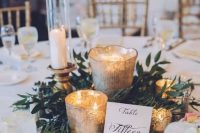 a romantic Christmas wedding centerpiece of greenery, mercury glass candleholders, a card and candles in glasses