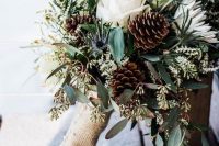a rustic Christmas wedding bouquet of white roses, thistles, pinecones and greenery is beautiful
