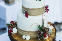 a rustic Christmas wedding cake with burlap ribbons, snowy pinecones, berries, leaves and some blooms is a pretty thing