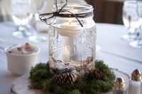a rustic Christmas wedding centerpiece of a tree slice, moss, pinecones and a jar with pebbles and a floating candle is gorgeous