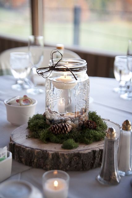 a rustic Christmas wedding centerpiece of a tree slice, moss, pinecones and a jar with pebbles and a floating candle is gorgeous