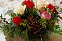 a rustic Christmas wedding centerpiece of a wooden box with greenery, red, pink and white blooms, pinecones and a glitter table number
