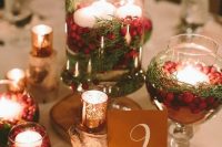 a rustic Christmas wedding centerpiece of glasses with cranberries, greenery and floating candles, wood slices and mercury glass candleholders