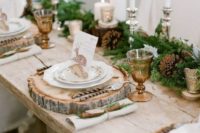 a rustic Christmas wedding tablescape with an evergreen and pinecone runner, various candles and wood slice placemats