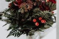 a rustic and bold Christmas wedding centerpiece of a jar with greenery, ferns, berries and red roses is amazing
