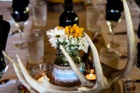 a rustic fall wedding centerpiece of a wood slice, antlers, simple blooms in a jar and candles is great for the fall