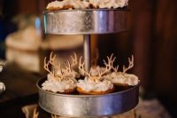 a rustic metal tiered stand with cupcakes topped with wooden antlers is a perfection for a woodland or rustic wedding