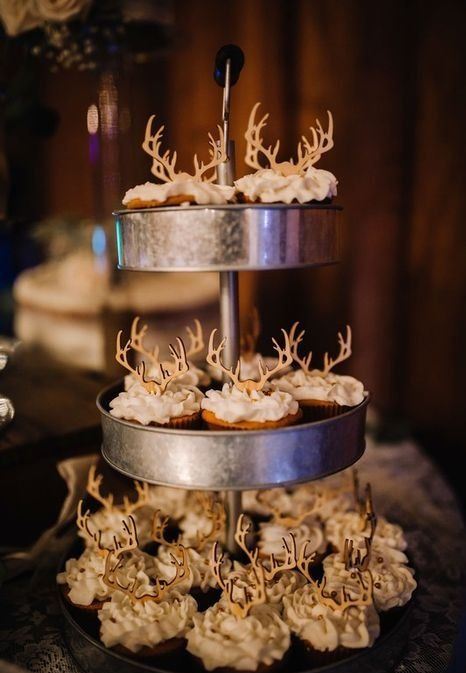 a rustic metal tiered stand with cupcakes topped with wooden antlers is a perfection for a woodland or rustic wedding