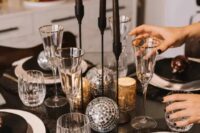 a shiny NYE wedding centerpiece composed of disco balls, tall and thin black candles in black candleholders and usual gold candleholders