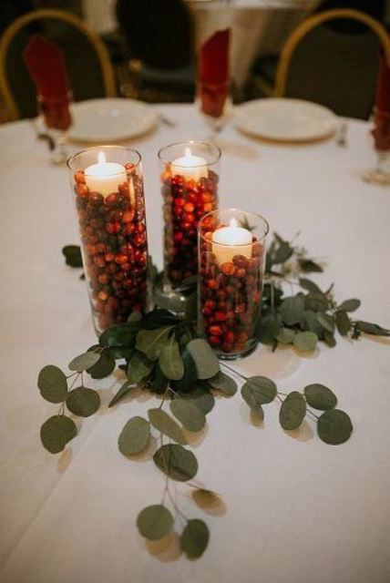 a simple rustic Christmas wedding centerpiece of tall glass vases with cranberries, candles and greenery is a cute and easy idea