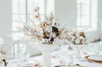 a snowy Christmas wedding centerpiece of a white vase with botton, dried herbs and white blooms and branches