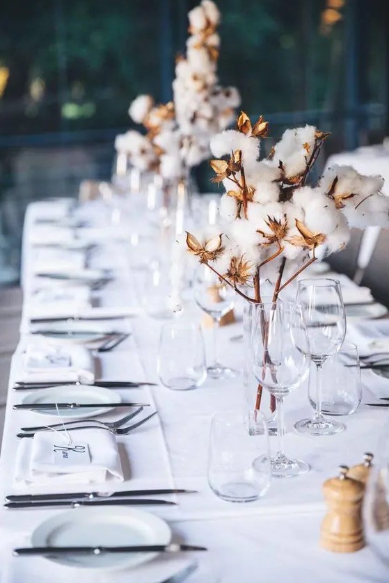 a stylish and cozy winter wedding table setting done in white and with cotton on branches for centerpieces is chic and cool