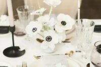 a stylish minimalist winter wedding tablescape with a white anemone centerpiece, neutral porcelain and a floral menu, black candleholders and cutlery