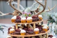 a tiered wedding dessert stand with blooms, greenery, antlers and lots of cupcakes is perfect for any woodland wedding