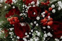 a traditional Christmas wedding bouquet of red roses, berries, greenery and baby’s breath is contrasting