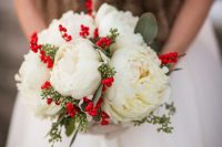 a traditional Christmas wedding bouquet of white peonies, red berries and greenery is bold and cool