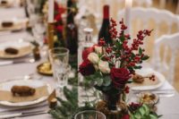 a traditional and chic Christmas tablescape with evergreens, greenery, white and red roses and berries, pinecones and tall and thin candles