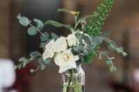 a very cool and easy wedding centerpiece of white roses, euclayptus and fern in a sheer vase and candles
