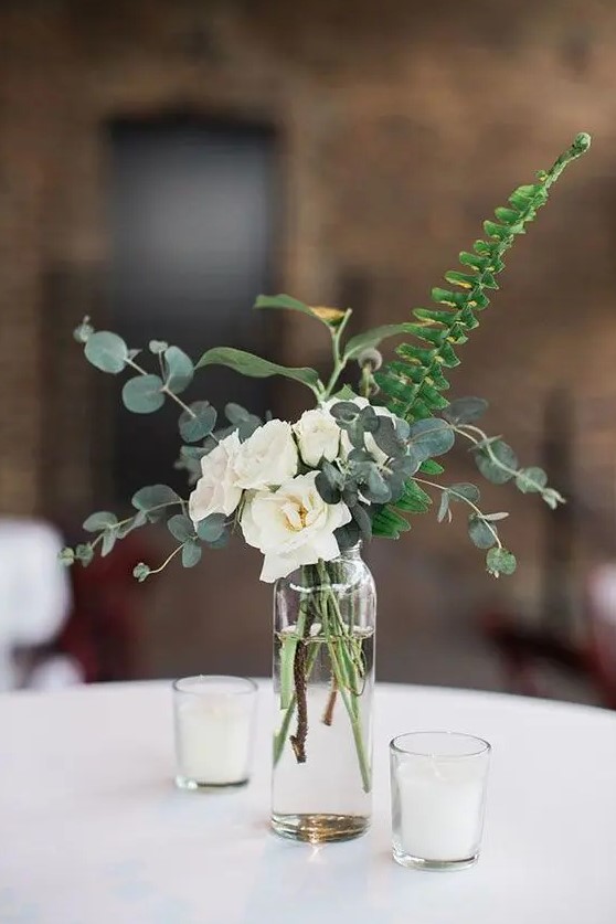 a very cool and easy wedding centerpiece of white roses, euclayptus and fern in a sheer vase and candles