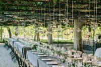 a vineyard wedding reception with grey tablecloths and greenery runners with pink blooms, small candles and bubbles with candles over the tables