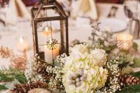 a vintage and rustic Christmas wedding centerpiece of greenery, fir branches, baby’s breath, white blooms and a vintage lantern with a candle