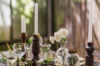 a vintage botanical wedding centerpiece of greenery, white blooms and berries in vases and jars and tall and thin candles