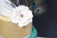 a wedding cake in gold, blue, white, with a sugar bloom and peacock feathers for decor