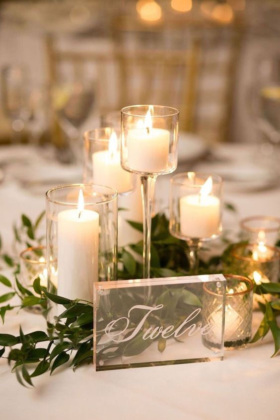a wedding centerpiece of candles in glasses, greenery and acryl is amazing for a wedding