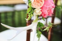 a wedding chair decorated with antlers, greenery, peachy and bright pink blooms is a bold and chic idea