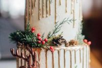 a white wedding cake with gold drip, fir twigs, pinecones, a glitter deer and cinnamon sticks is a very Christmassy piece