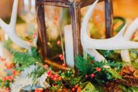 a winter wedding centerpiece of greenery, berries, pinecones, feathers, antlers and a candle lantern in the center