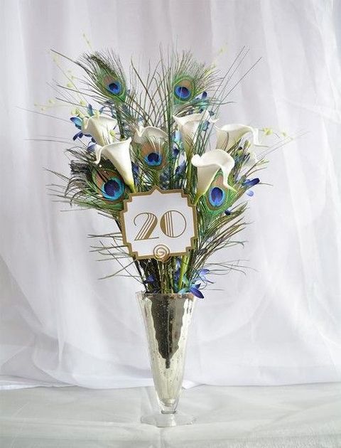 an art deco wedding centerpiece with peacock feathers and white callas plus a table number