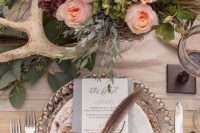 an elegant vintage woodland wedding centerpiece of peachy blooms, greenery, feathers and antlers is a gorgeous idea for a more formal wedding