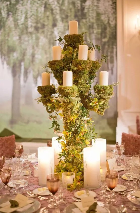 an enchanted forest wedding centerpiece of a large candelabra covered with moss and green orchids and with pillar candles