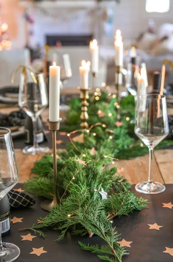 an evergreen table runner dotted with LED lights and elegant tall and thin candles is a stylish idea for a NYE wedding