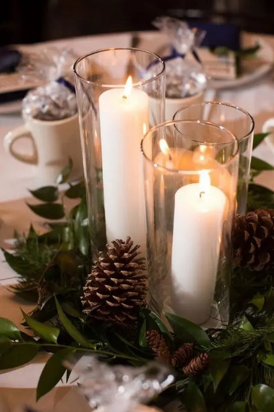 an inspiring winter wedding centerpiece of greenery, pinecones and pillar candles in tall glasses is a great idea for winter