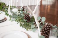 elegant winter woodland wedding table decor with a greenery, pinecone and antler runner and some floating candles in glasses