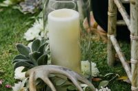 wedding aisle decor with white blooms, greenery, succulents, antlers and a large candle in a glass is beautiful