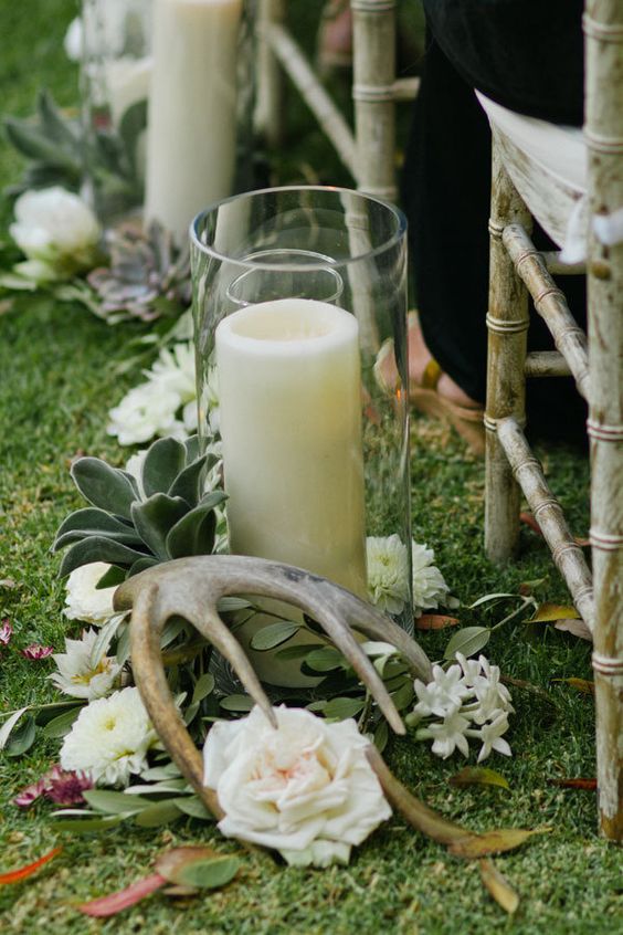 wedding aisle decor with white blooms, greenery, succulents, antlers and a large candle in a glass is beautiful