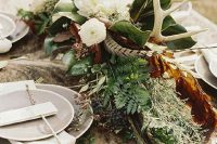 wedding table decor done with greenery, dried leaves, white blooms, privet berries and antlers plus faux fur on the table