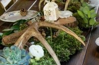 woodland wedding table decor with moss, succulents, pinecones, antlers, greenery and a tiny candle lantern on top