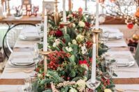 a Christmas wedding tablescape with a greenery and fir runner, with berries and red roses, candles and gold cutlery