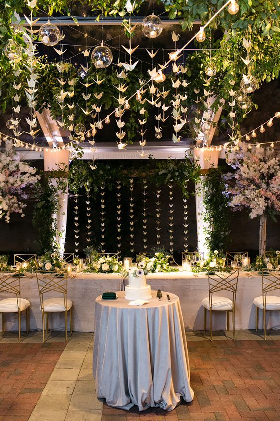 a beautiful neutral reception space with lots of greenery, bubbles with candles and white paper cranes, white floral centerpieces on the tables