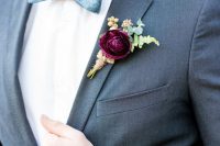 a bold purple bloom, berry and greenery boutonniere is a colorful accent for a winter groom’s look done in grey and blue