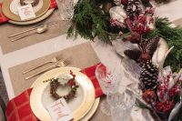 a bold winter or Christmas wedding tablescape with berries, pinecones, candles, fit, red candles, mini wreaths and gold cutlery