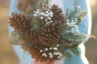 a bouquet made of large pinecones, evergreens and baby’s breath for a rustic winter bride