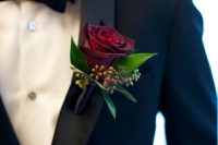 a burgundy rose boutonniere with leaves and berries is a bold touch to a classic black tux look
