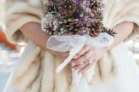 a catchy organic wedding bouquet of pinecones and lilac blooms in a tulle wrap is a stylish idea for a winter wedding