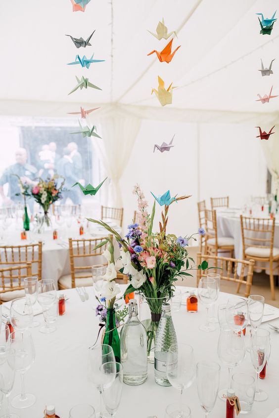 a chic neutral wedding reception spruced up with bright blooms and greenery and colorful paper cranes over the tables