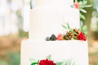 a chic white wedding cake with pinecones, fir, blooms, berries, greenery and fun calligraphy toppers